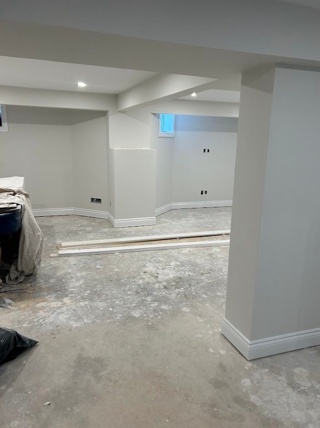 Basement under construction; walls painted light gray, concrete floor, baseboards installed.