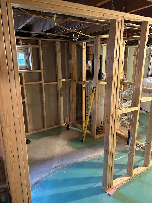 Basement framing with wooden studs, unfinished walls, and electrical wiring. Turquoise floor and a window are visible.