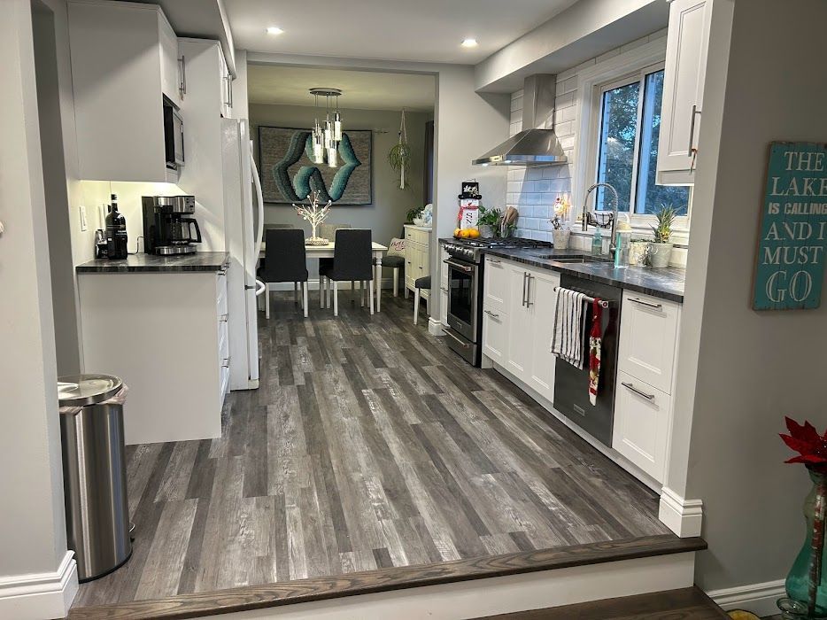 Kitchen with white cabinets, gray countertops, and wood-look flooring. A dining room is visible in the background.