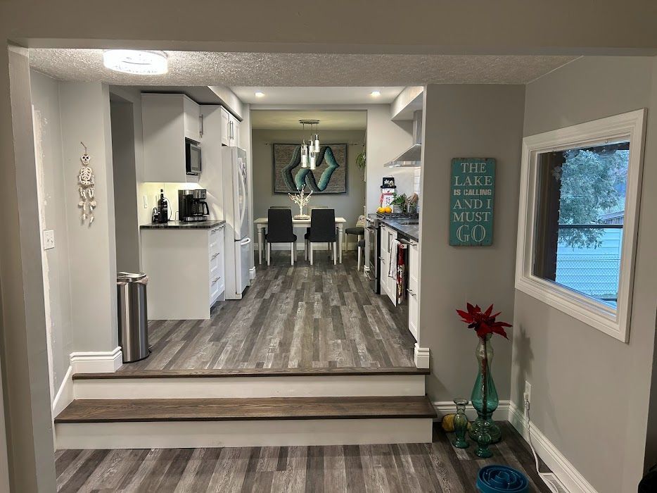 Interior view with kitchen, dining area, and living space; gray walls, wood-look flooring, and a window.