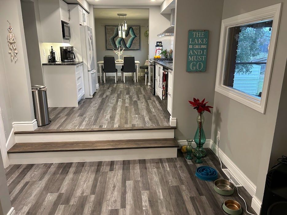 Kitchen with wood-look flooring, leading to dining area. Raised floor, white cabinets, and a decorative sign.