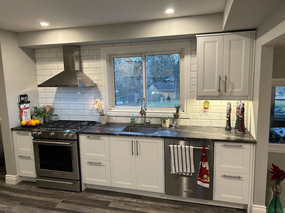 A kitchen with white cabinets , stainless steel appliances , a sink , and a window.