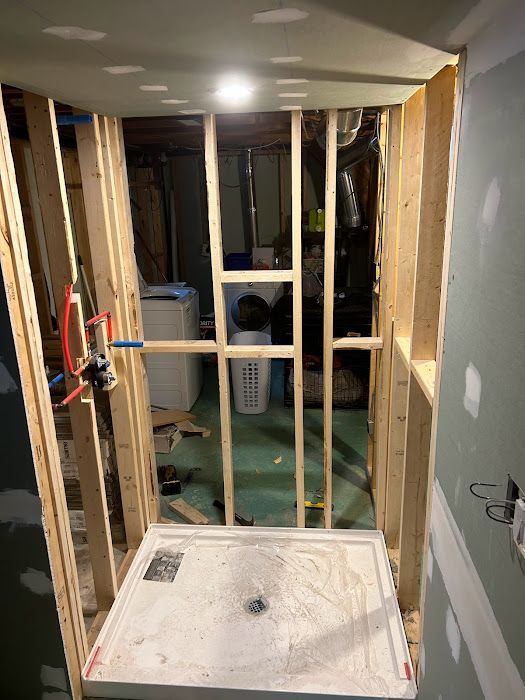 Framed shower stall under construction; white shower pan installed, plumbing visible.