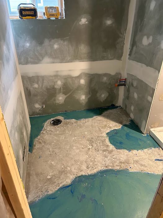 Bathroom under construction; green waterproofing layer on floor, exposed studs, partially finished walls.