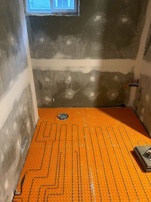 Orange floor heating mat installed in a shower. Walls are grey and unfinished.