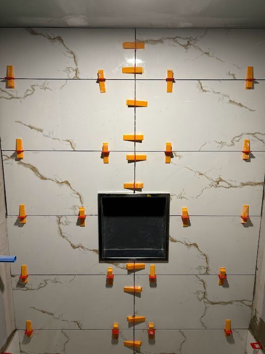 Tiled bathroom wall with orange leveling clips; a black recessed shelf is centered.