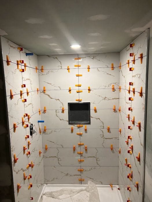 Shower stall with white marble-like tiles being installed; orange tile leveling clips visible.