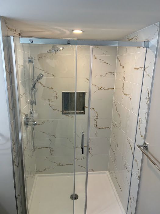 Modern shower with marble-look tiles, glass sliding door, and chrome fixtures.