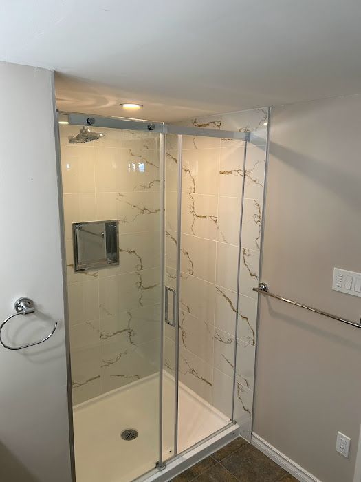 A modern shower with clear glass doors, white marble-look tiles, and a chrome shower head and fixtures.