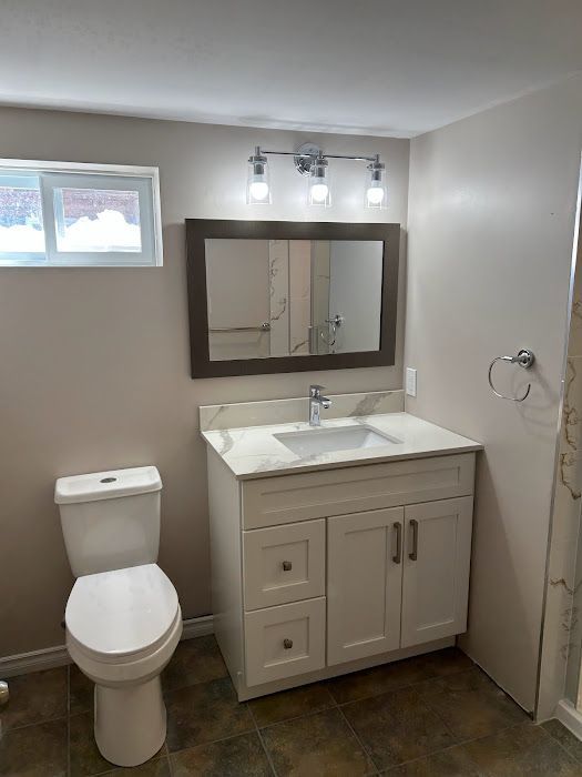 Bathroom with white vanity, toilet, and a window. Beige walls, mirror, and a three-light fixture.