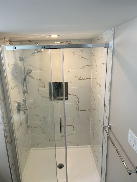 Modern shower with glass doors, white marble-look tile, chrome fixtures, and a recessed soap niche.