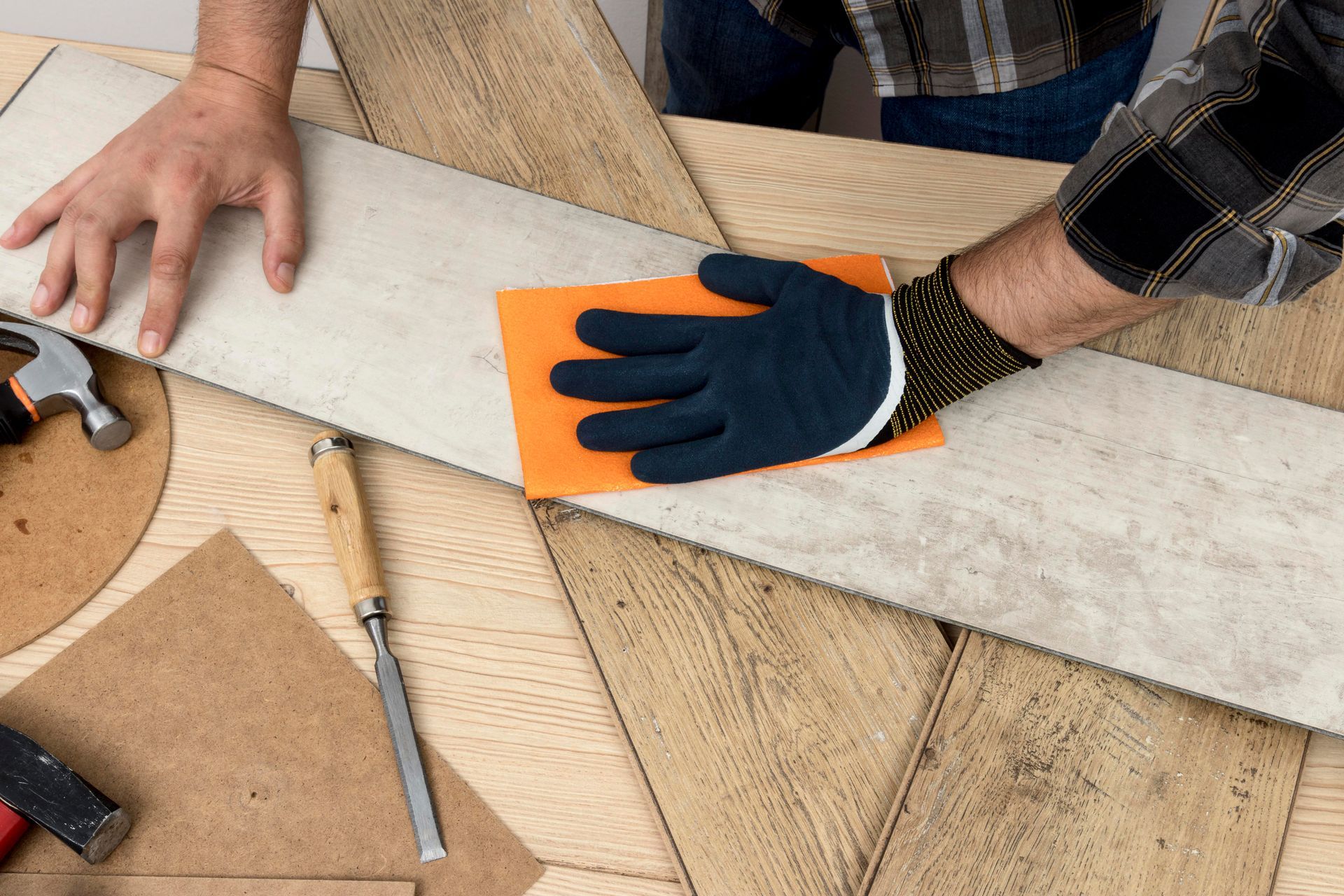Person sanding a light wood plank with an orange sanding block, on a wood table with tools.