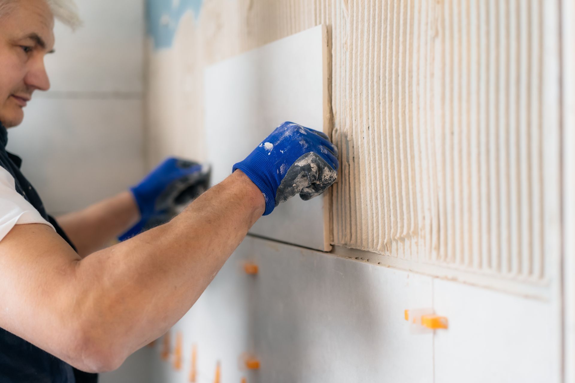 A man is installing tiles on a wall in a bathroom.