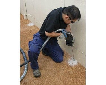 A man is kneeling down and using a drill on a wall.