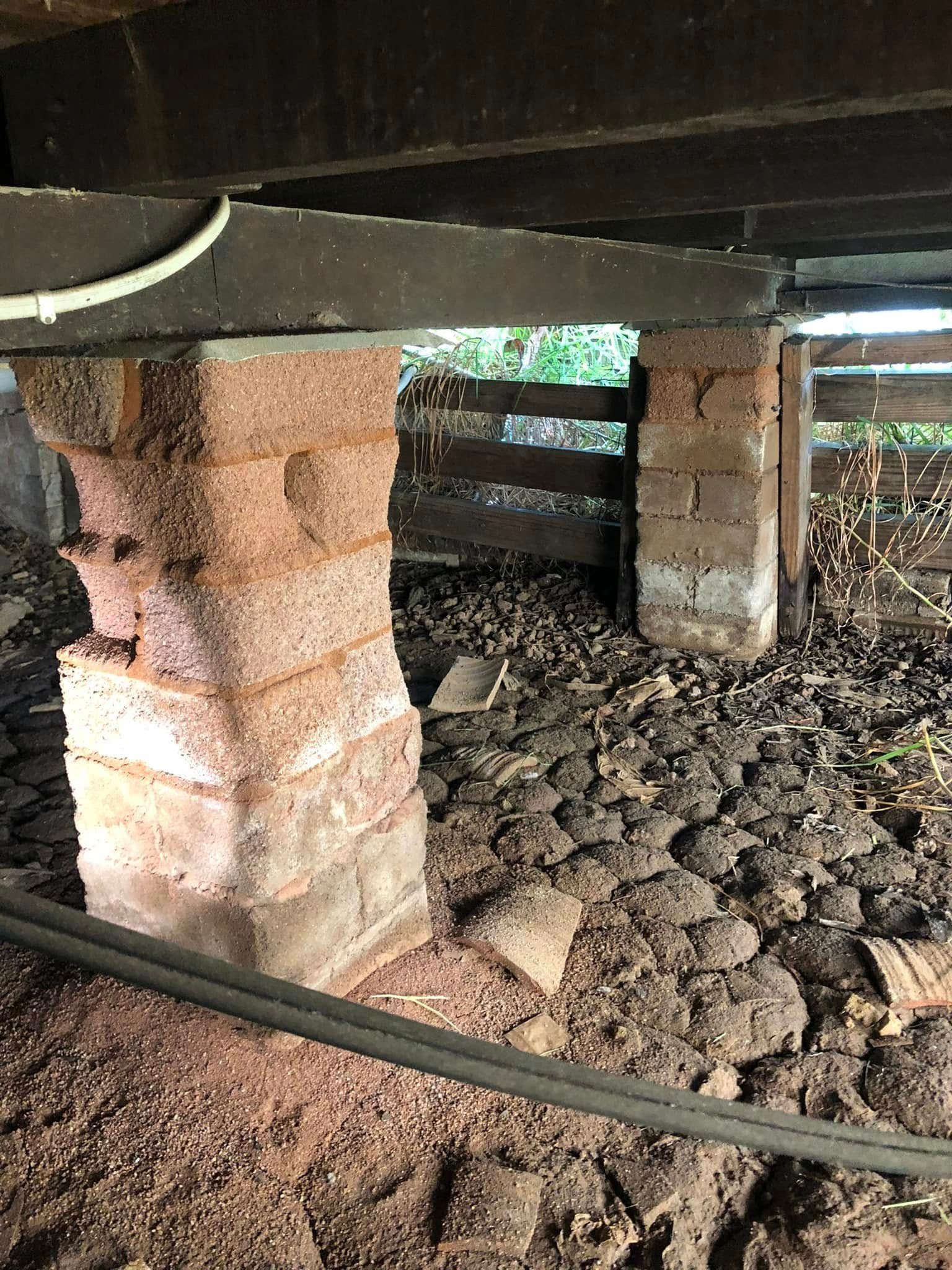 A brick column is sitting on top of a pile of dirt under a house.