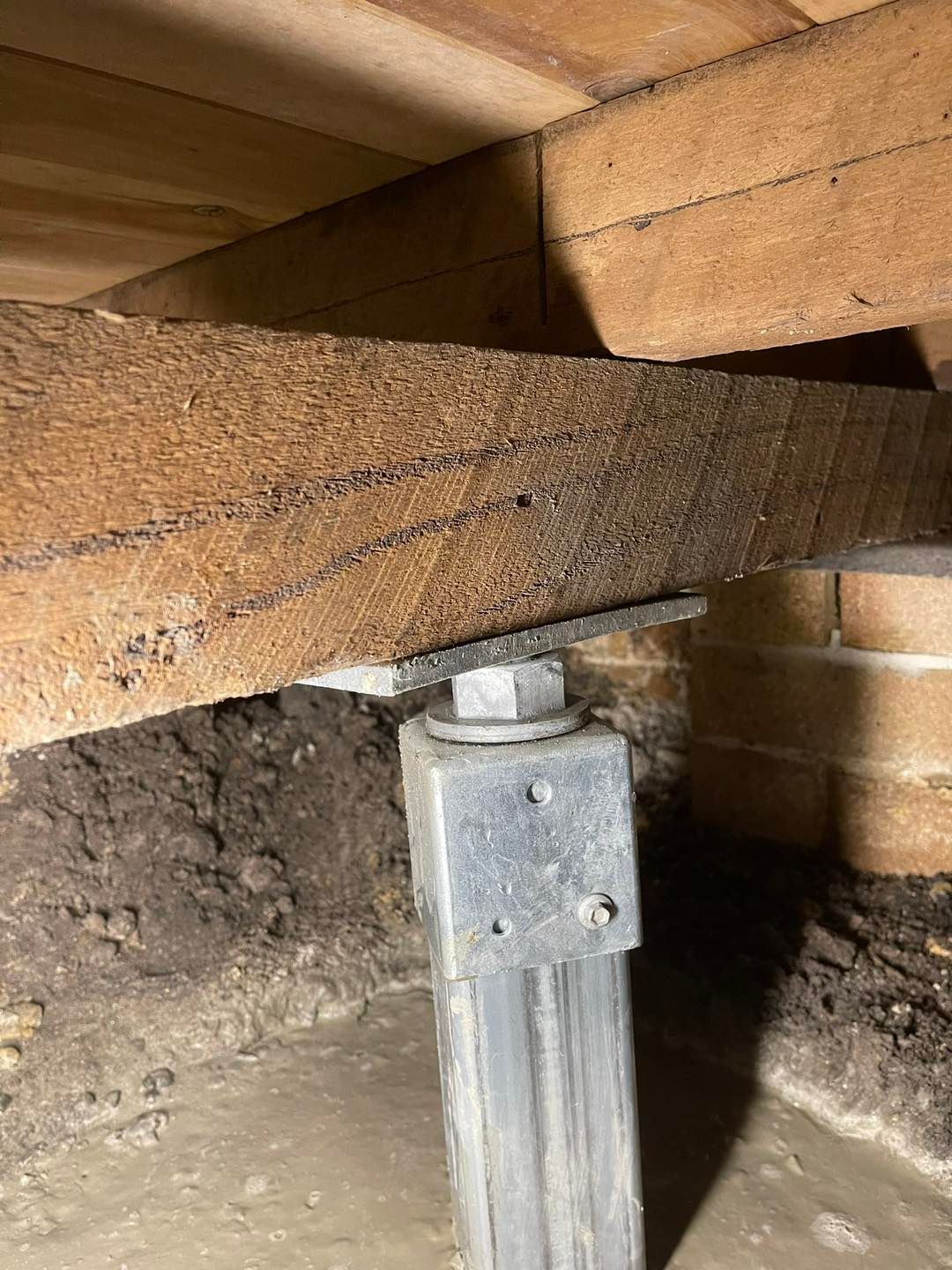 A wooden beam is sitting on top of a metal post in a basement.