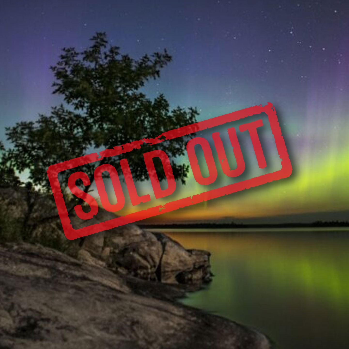 Vibrant green and purple aurora borealis illuminates the night sky above a calm, reflective lake and rocky shoreline.