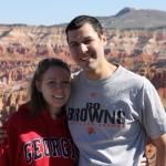 A smiling couple stands outdoors in front of a rocky canyon landscape, wearing a red Georgia sweatshirt and gray t-shirt.