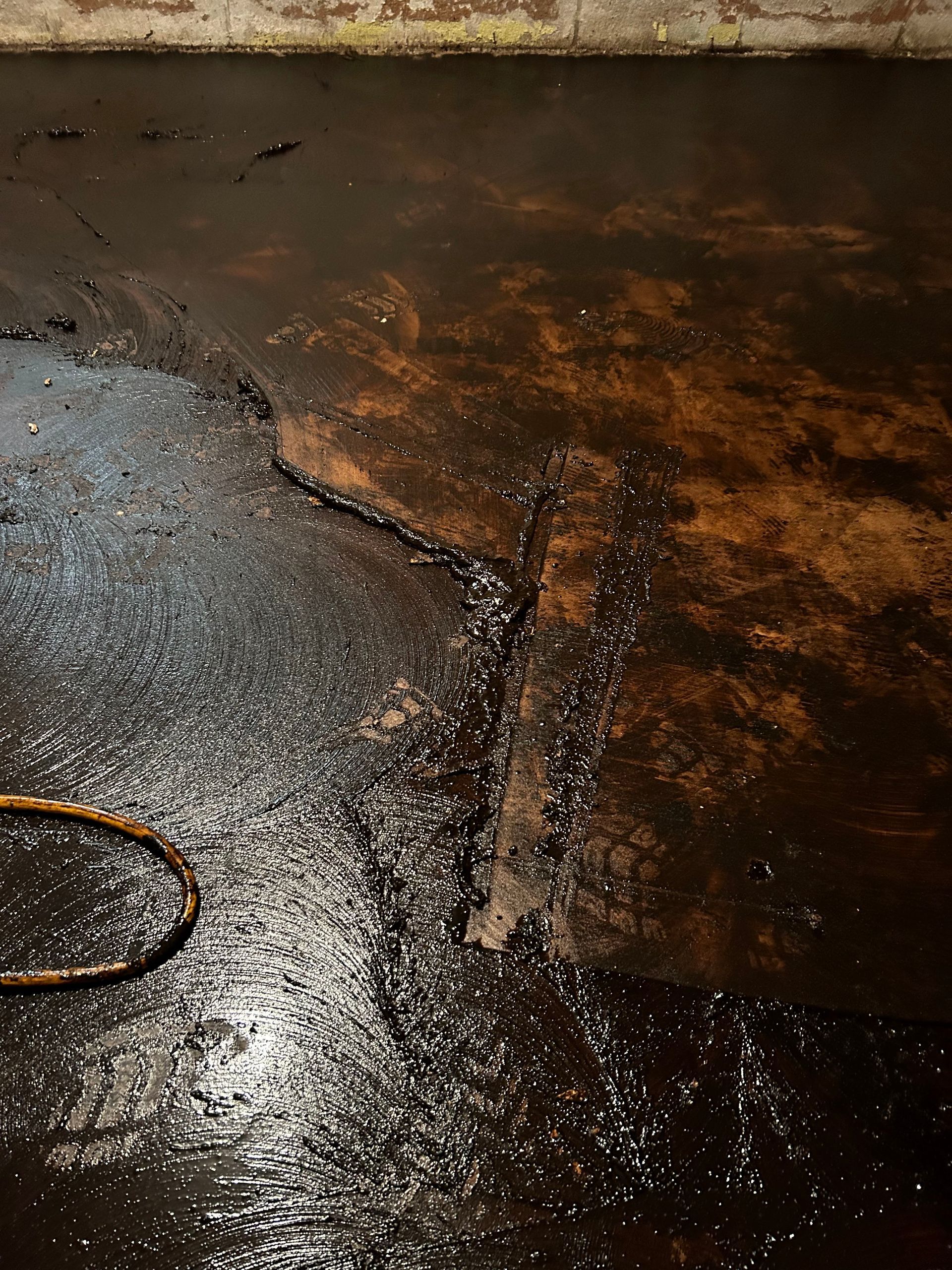 Dark, wet basement floor with crack and pooled water, possibly oil spill.