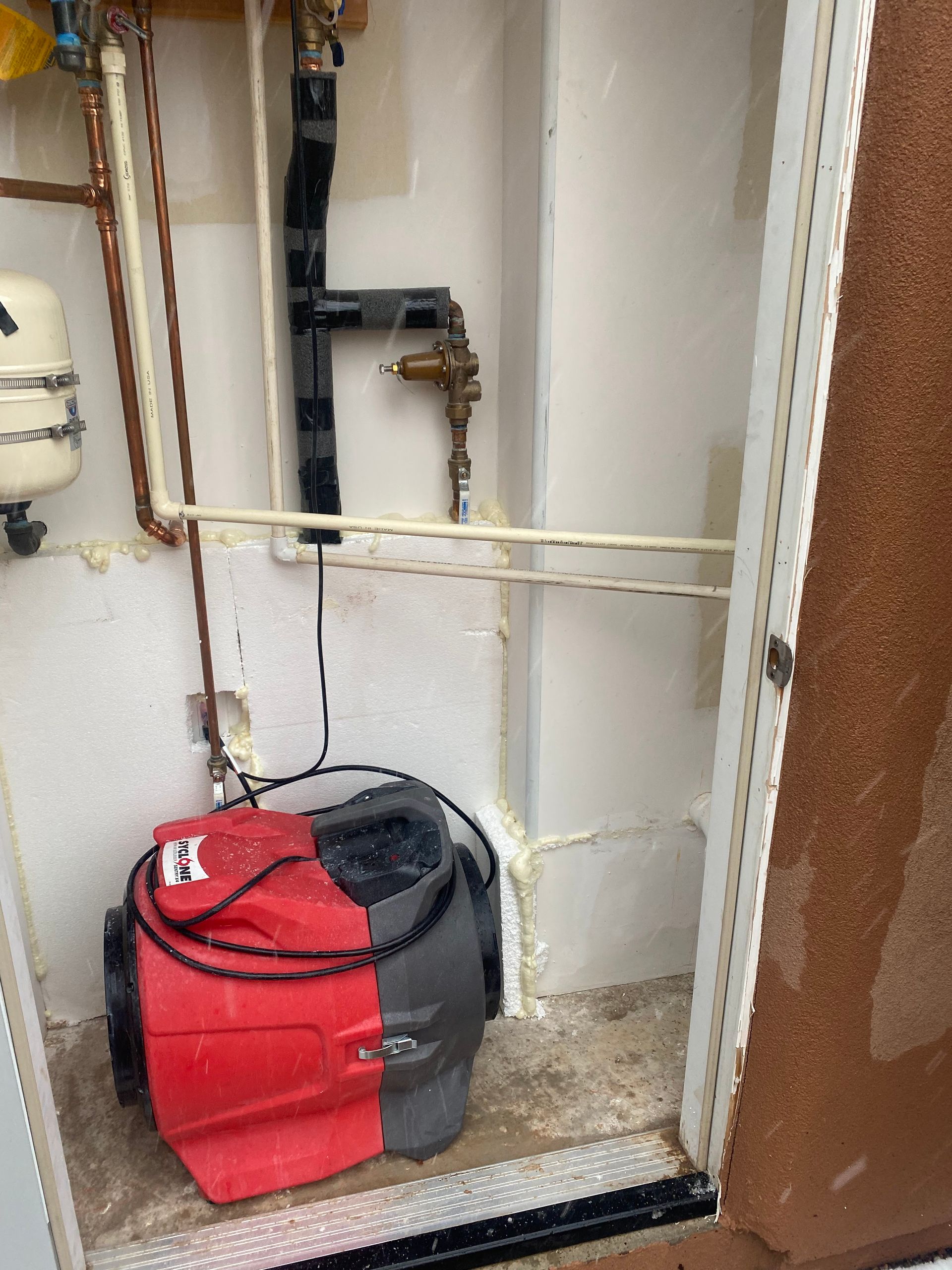 A red and gray pump sits in a utility room with copper pipes, a black pipe, and a white wall.