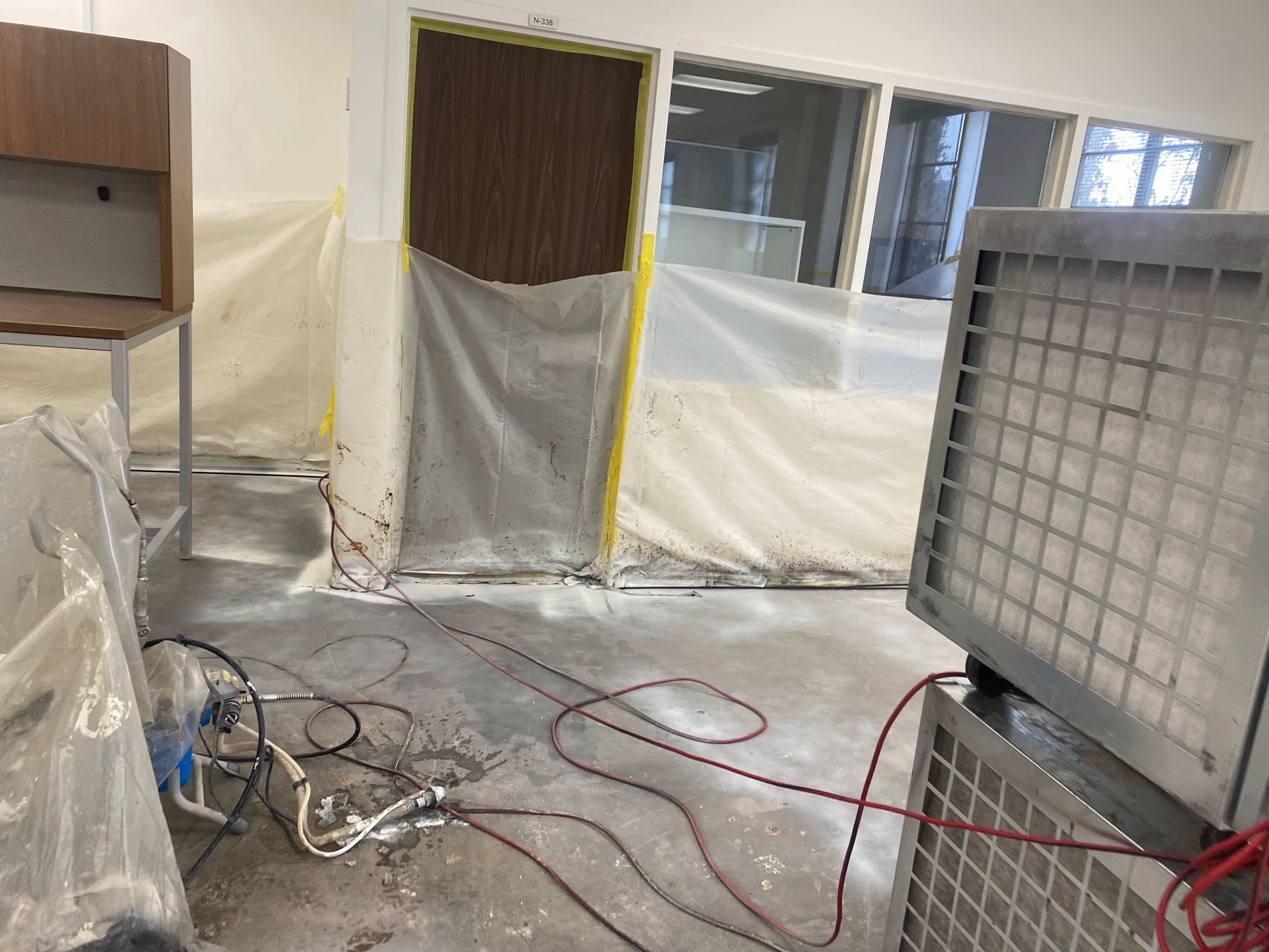 Interior construction site. Door and furniture covered in plastic. Air purifier and hoses on the floor.