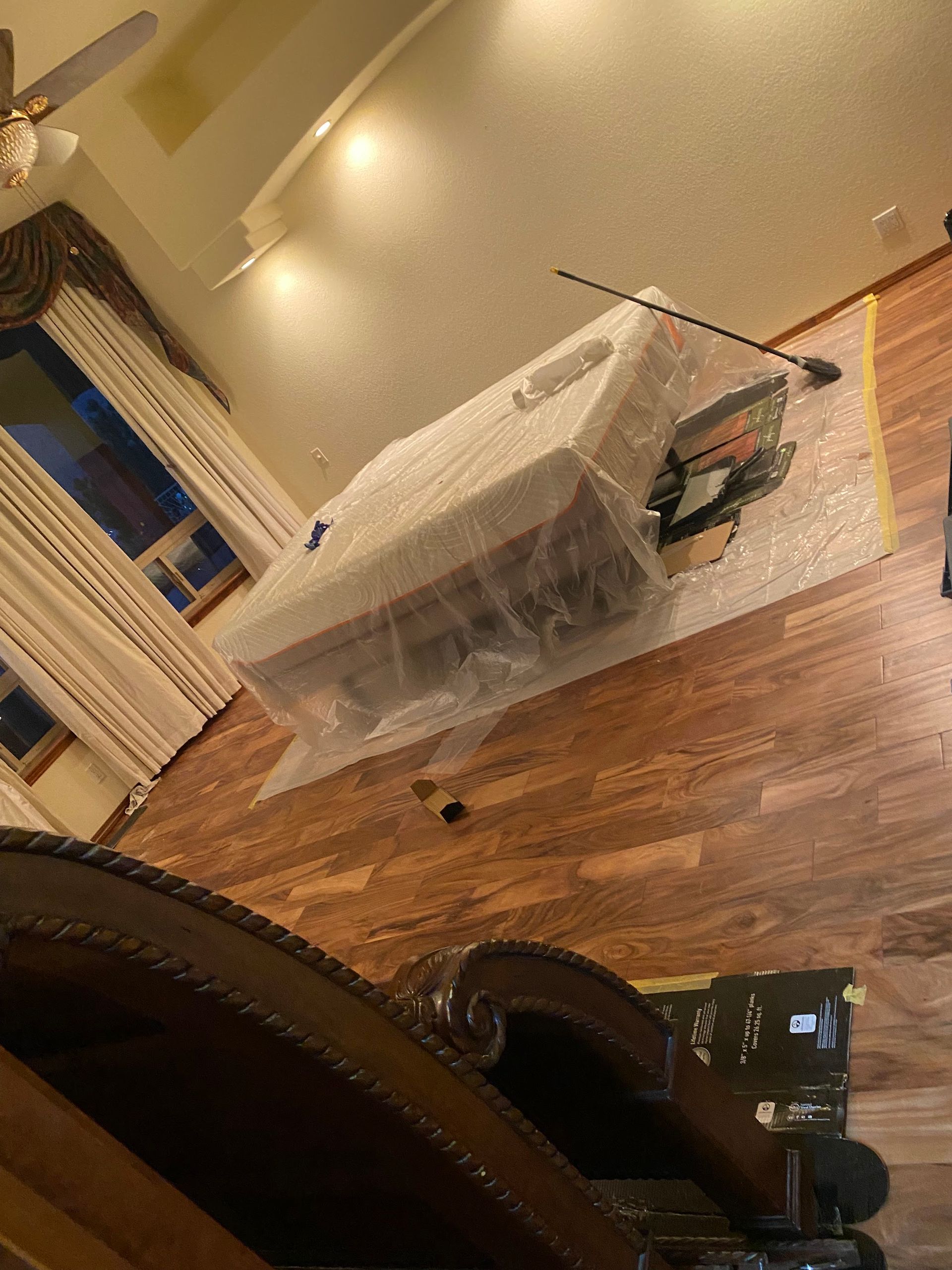 Table saw wrapped in plastic on a wood floor inside a house.