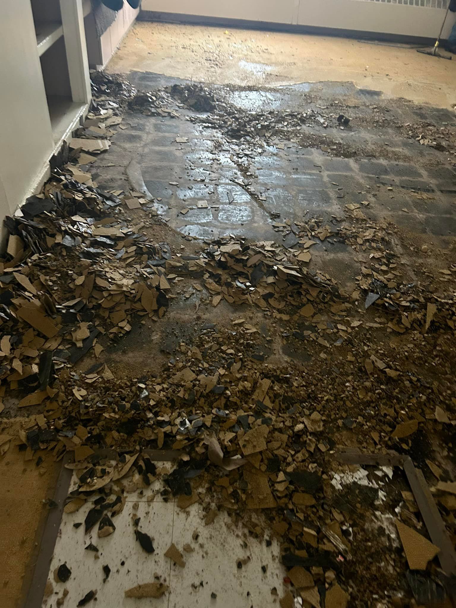 Debris and broken flooring cover a room's concrete floor, likely in renovation.
