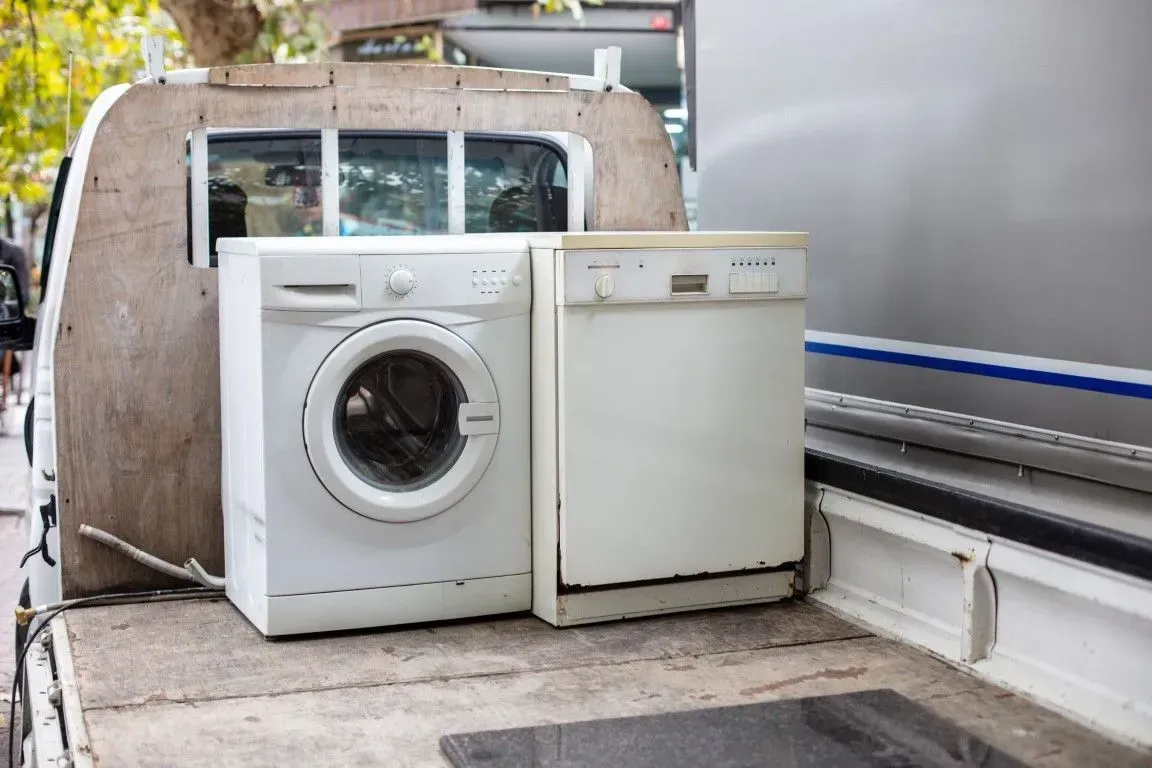 White washing machine and dishwasher loaded onto a pickup truck bed.