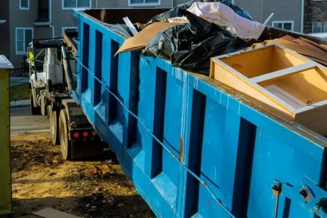 Blue dumpster being loaded onto a truck at a residential site.