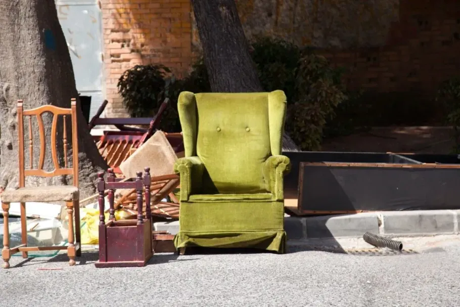 Old wooden chair and green armchair left on a curb for pickup.