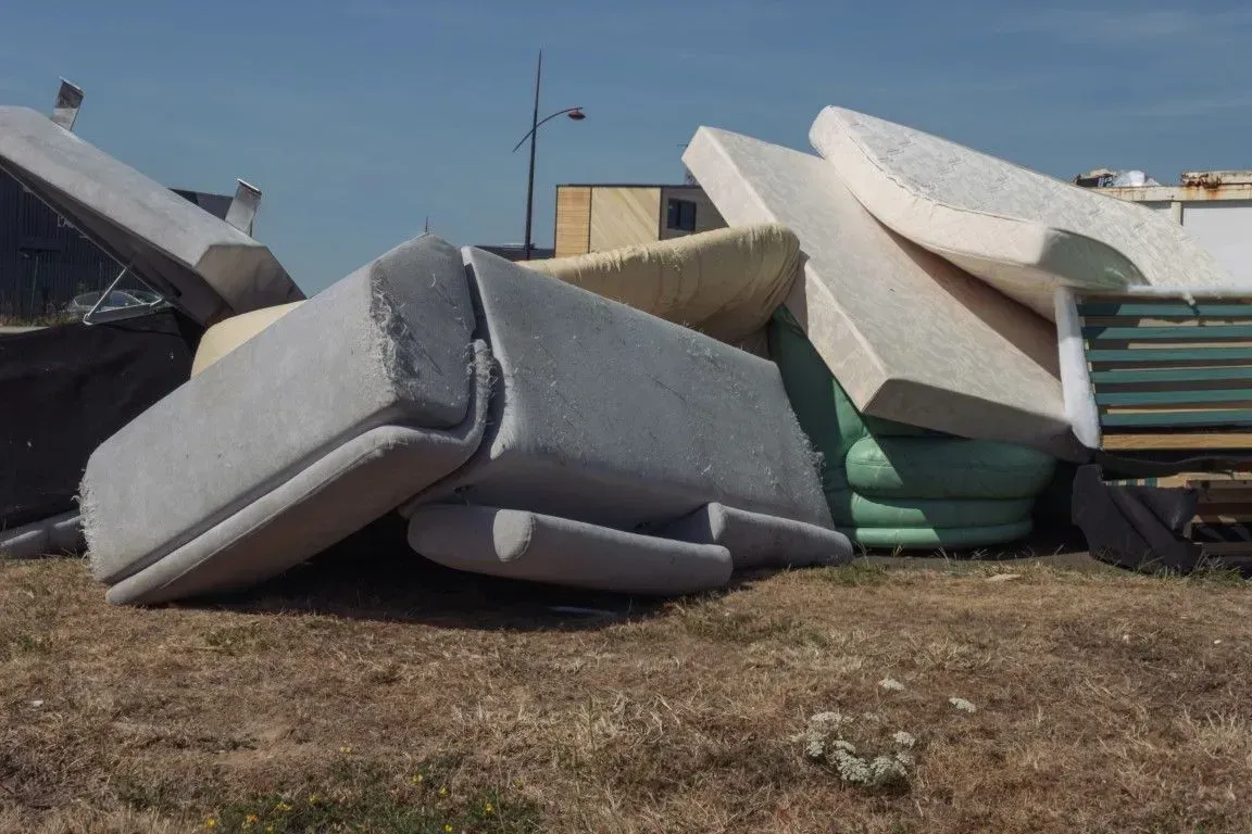 Pile of discarded sofa cushions and mattresses on the ground.