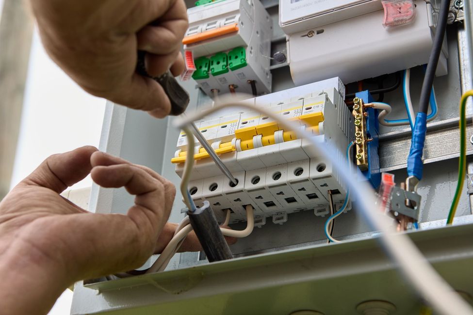 Hands wiring an electrical circuit panel with breakers and cables
