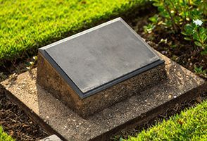 A gravestone is sitting on top of a concrete base in a cemetery.