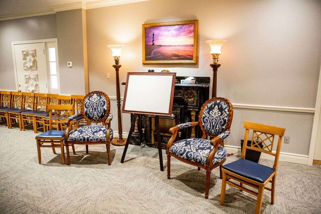 A room with chairs , an easel and a painting on the wall.