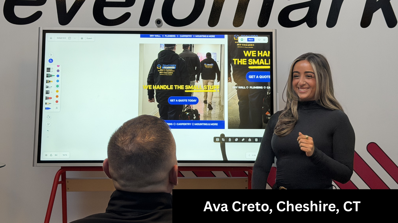 Woman presenting at a screen; Cheshire, CT. Screen shows ad. Man's back to camera; red and white setting.