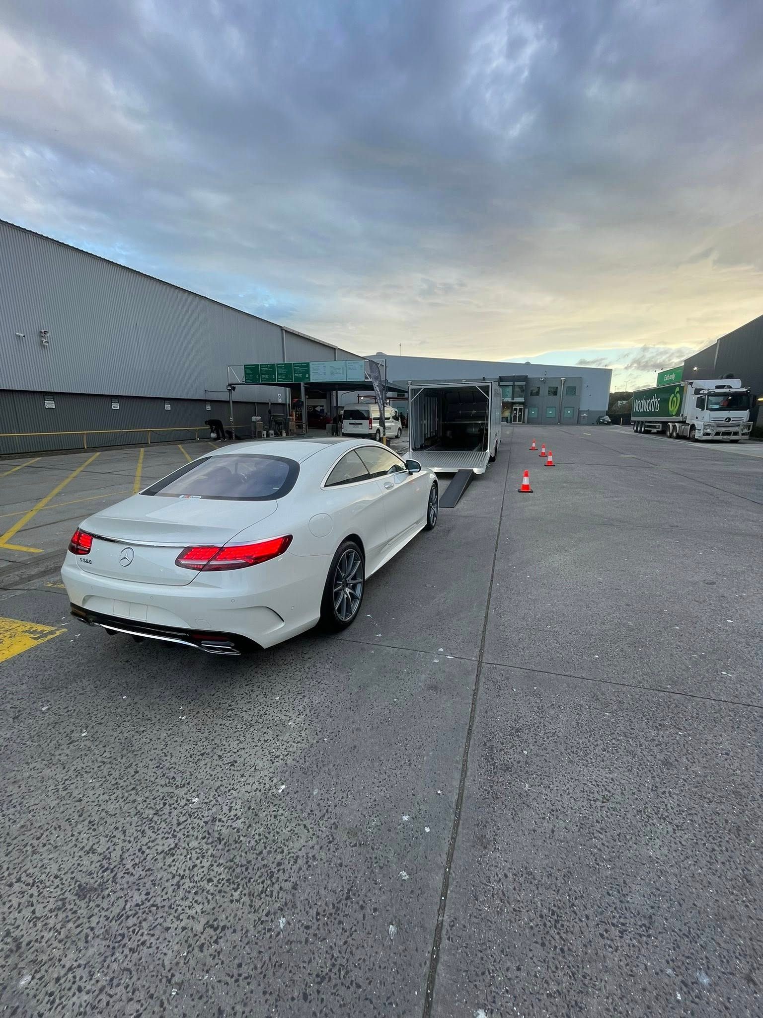 White Mercedes coupe on a trailer in an industrial area, under a cloudy sky — Full Throttle Enclosed Car Transport in Kilmore, VIC
