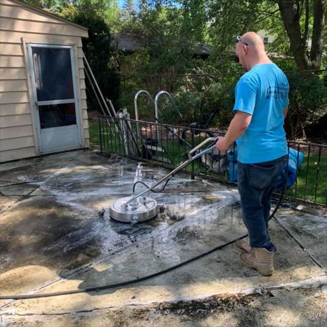 Pressure Pros Soft Washing LLC | man in a blue shirt is cleaning a patio with a machine.