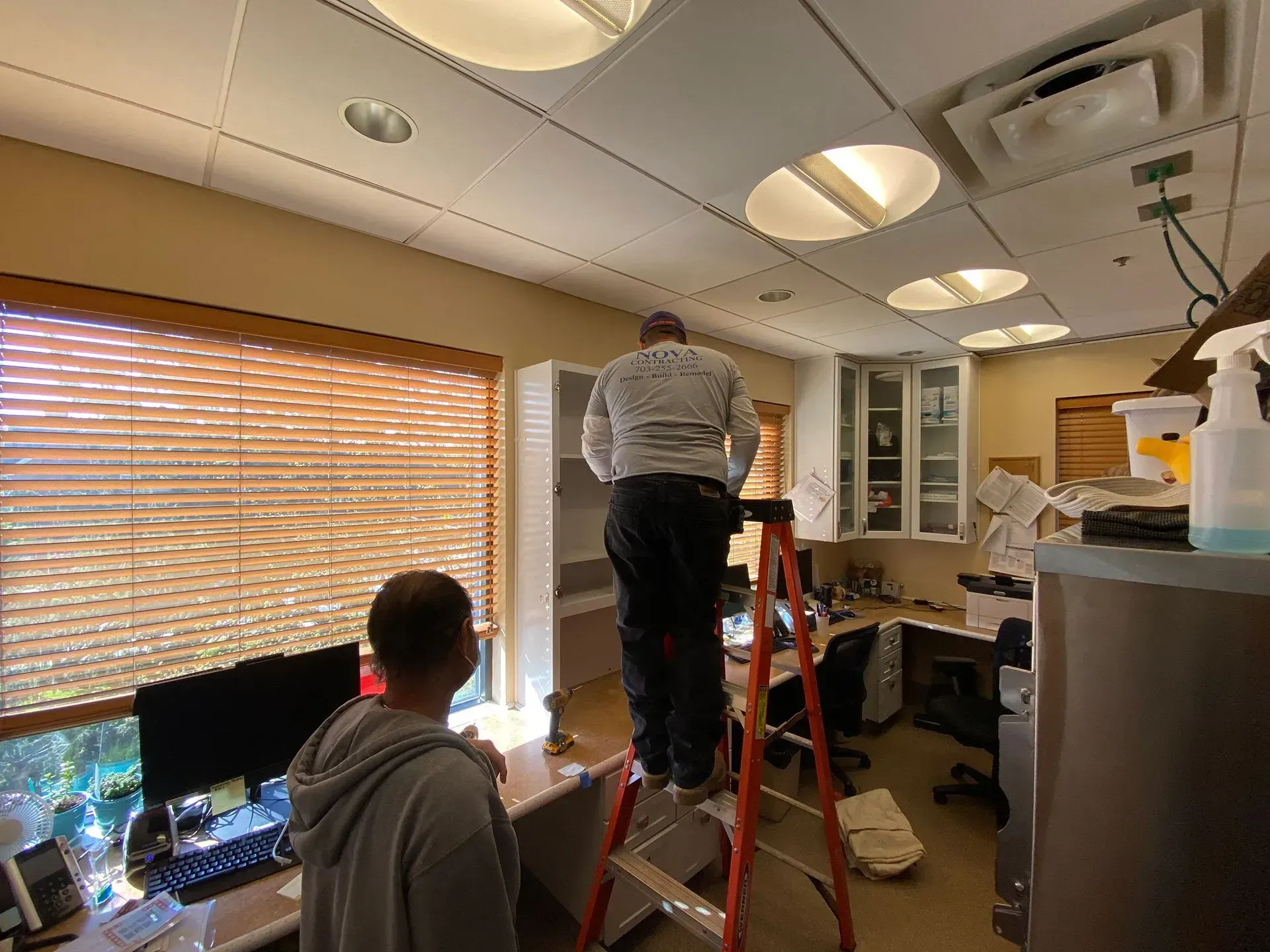 A man is standing on a ladder in an office.