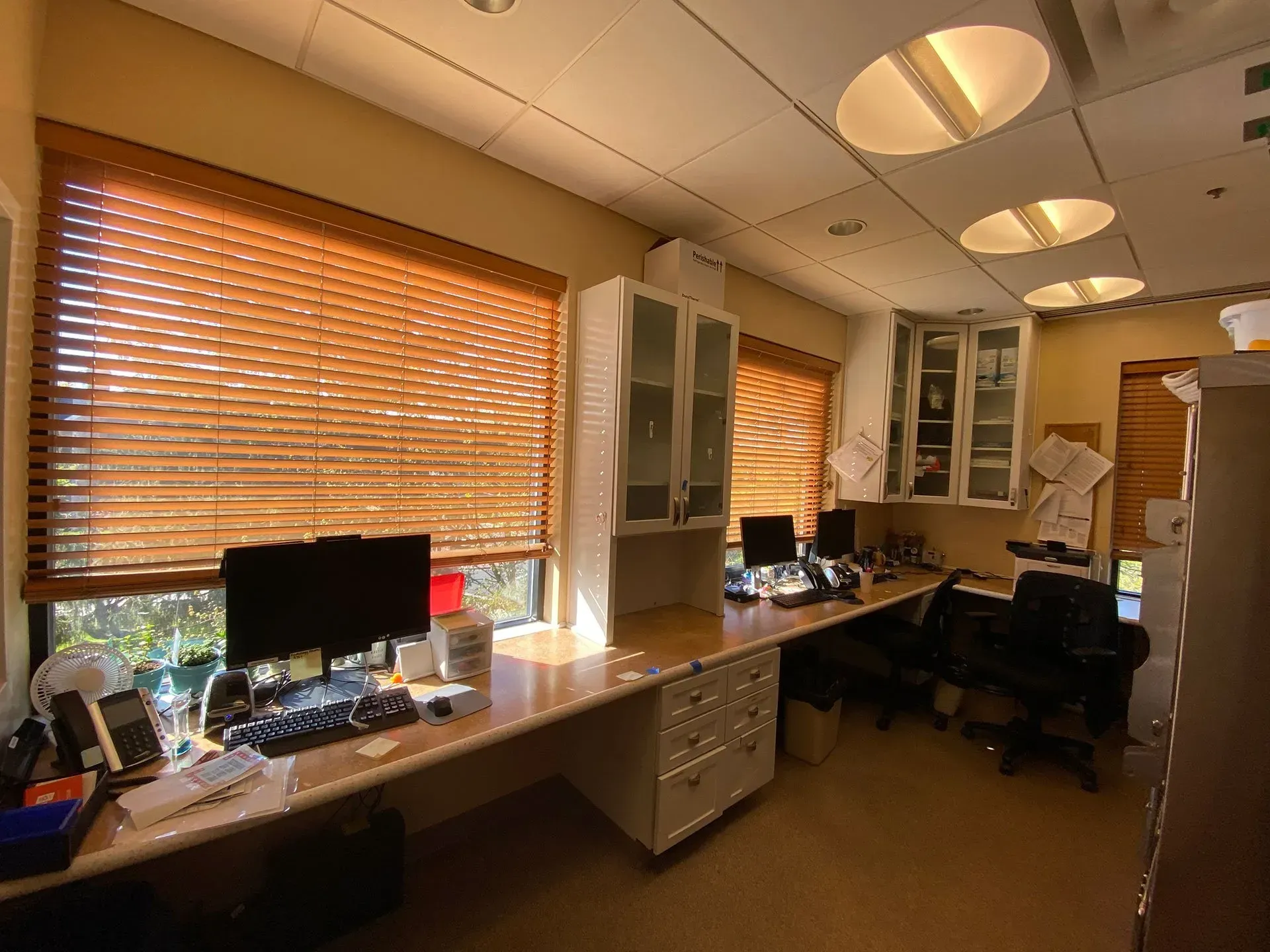 A room with a desk, chairs, computers and blinds.