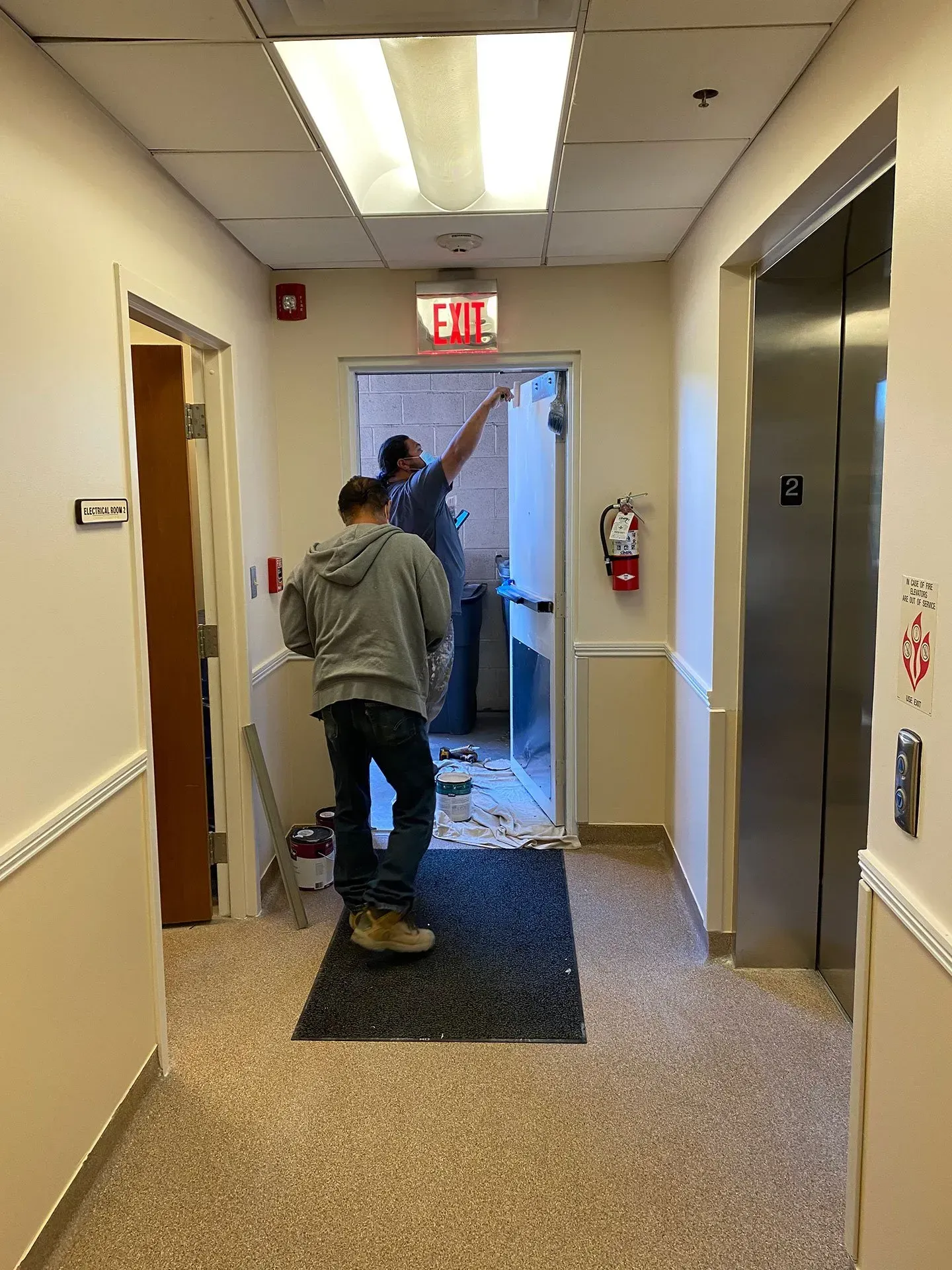A man is standing in a hallway next to an exit sign.