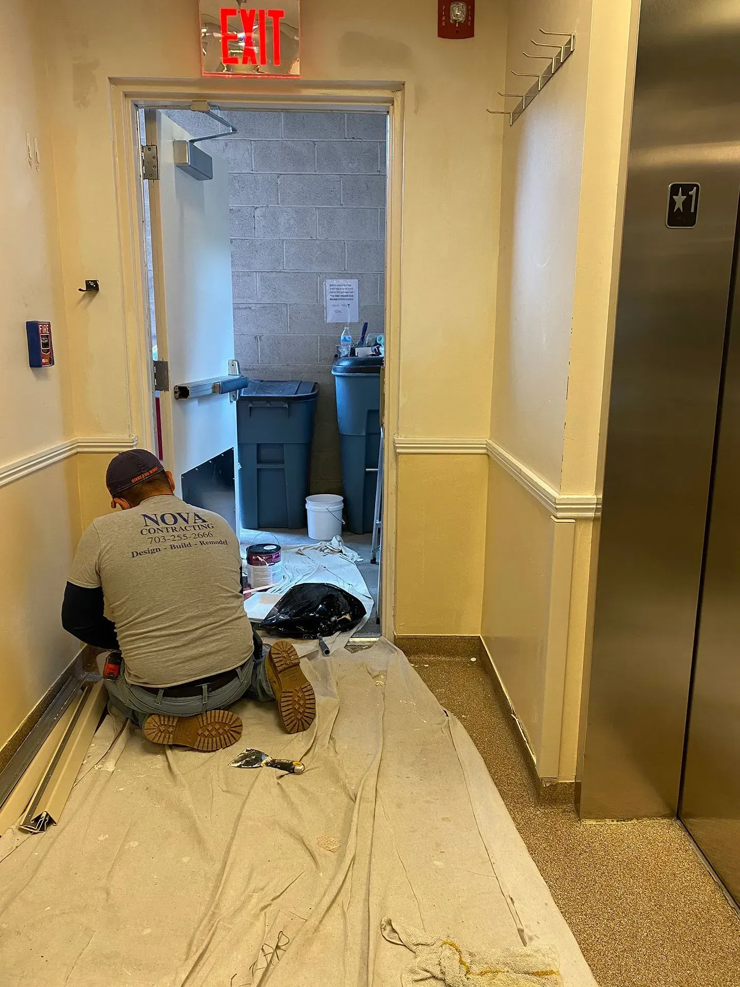 A man is kneeling on the floor in a hallway.