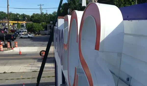 A large white sign with orange letters is being installed on the side of a building.