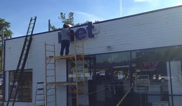 A man is standing on a scaffolding fixing a sign on the side of a building.