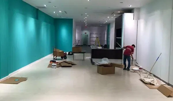 A man is cleaning the floor of an empty room with blue walls.