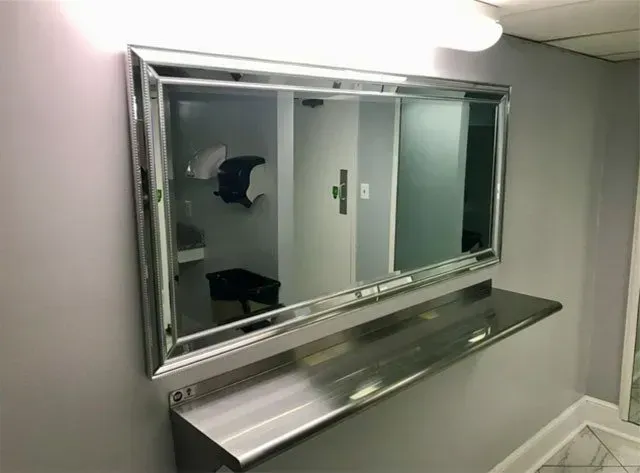 A large mirror is hanging on a wall next to a shelf.