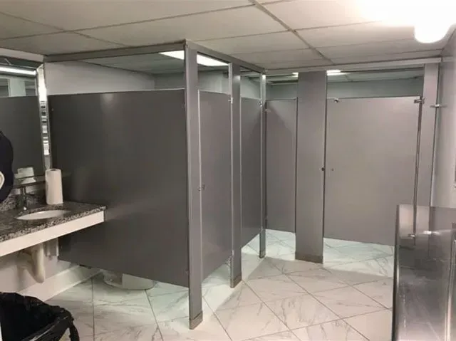 A public restroom with gray cubicles and a sink.