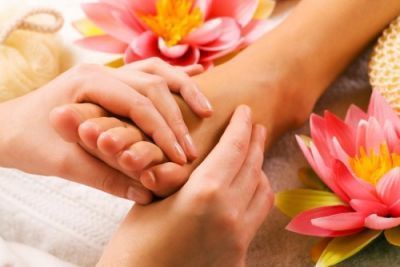 Hands massaging a foot, surrounded by pink flowers, suggesting a spa setting.