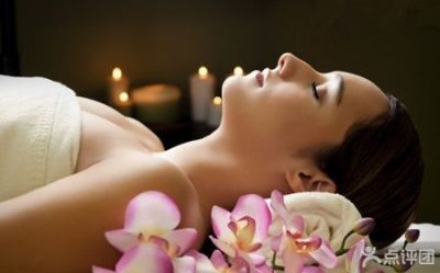 Woman relaxed during a spa treatment, laying on a table with candles and orchids in the background.