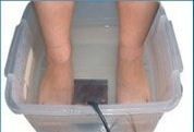 Feet in a plastic tub of water with a black device, for a foot detox.