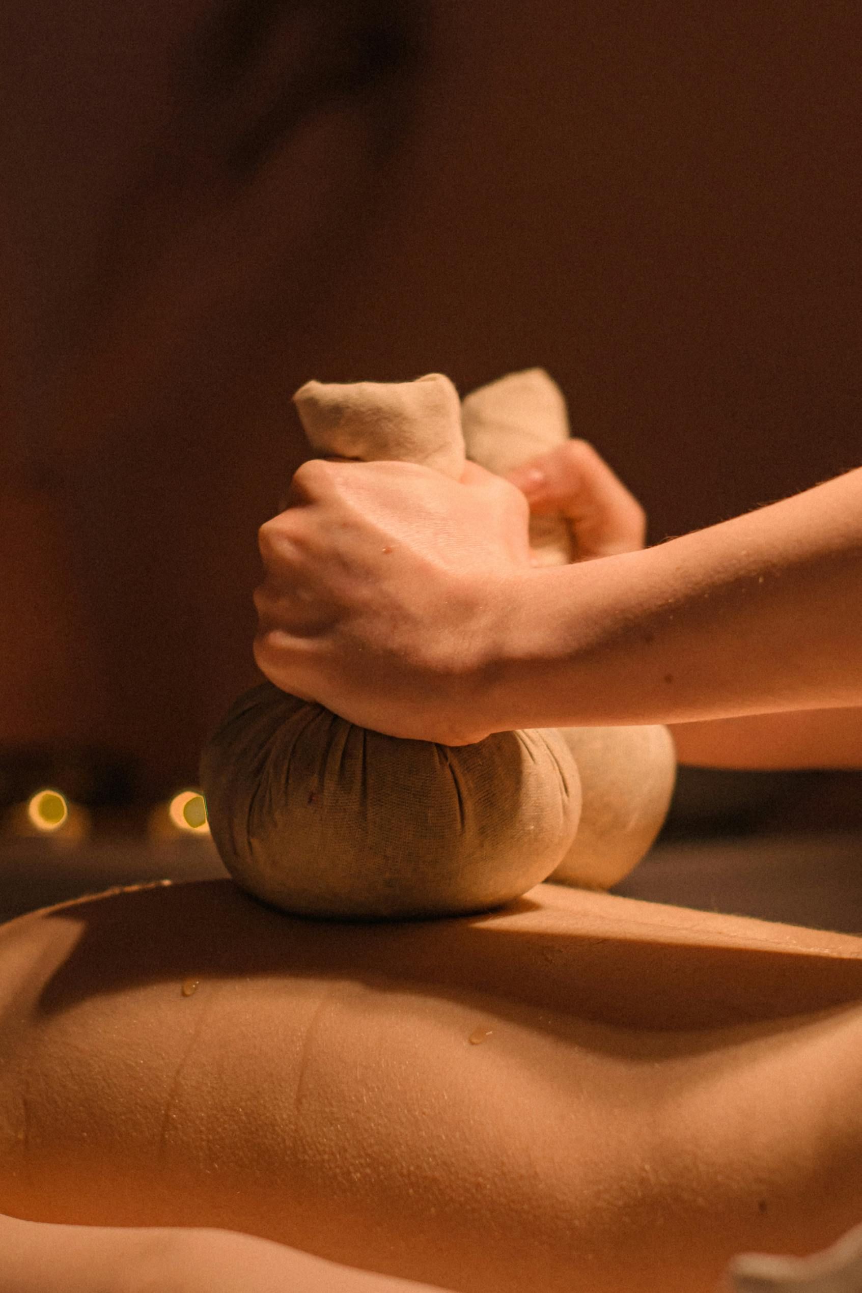 Hands pressing warm herbal compress balls onto a person's back, during a spa treatment.